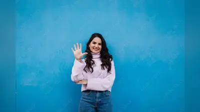 Smiling young beautiful woman showing number 5 in front of blue wall