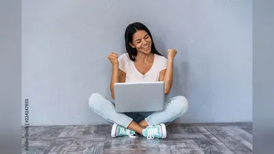 Portrait of excited young casual girl celebrating success while sitting with laptop computer isolated over gray background.